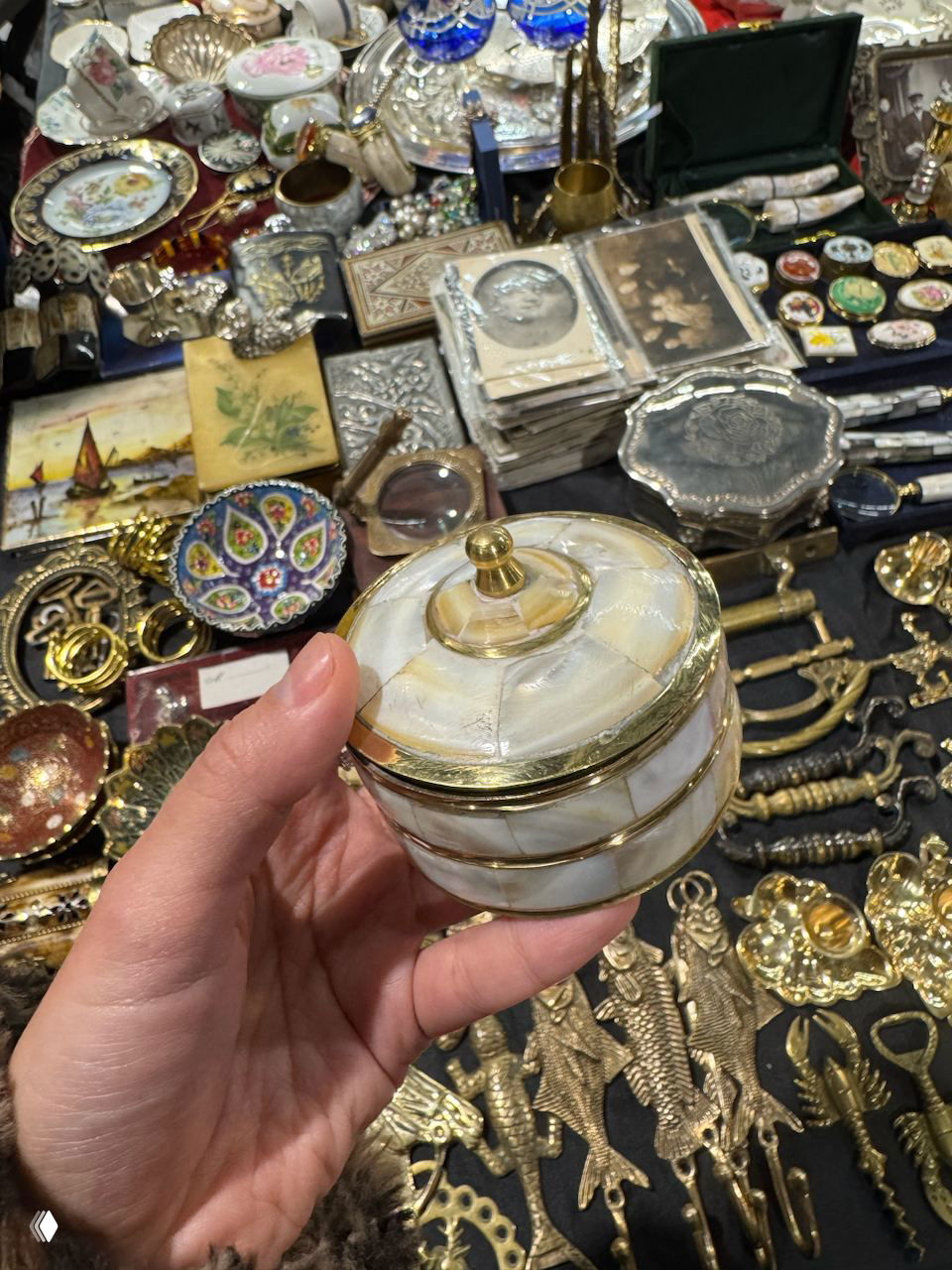 Рука держит перламутровую шкатулку с позолоченными вставками и крышкой — предмет, сделанный в Индии и выставленный среди антиквариата.