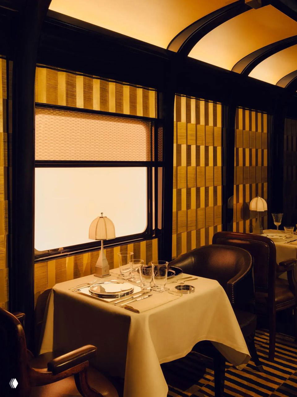 Ресторанный вагон с сервированными столиками, настольными лампами и стенами с геометрическим узором — классическое оформление столовой поезда.