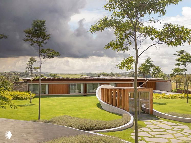 Общий ракурс капеллы и окружающего ландшафта: деревянные фасады, короткая одноэтажная постройка и волнообразные бетонные элементы по периметру.