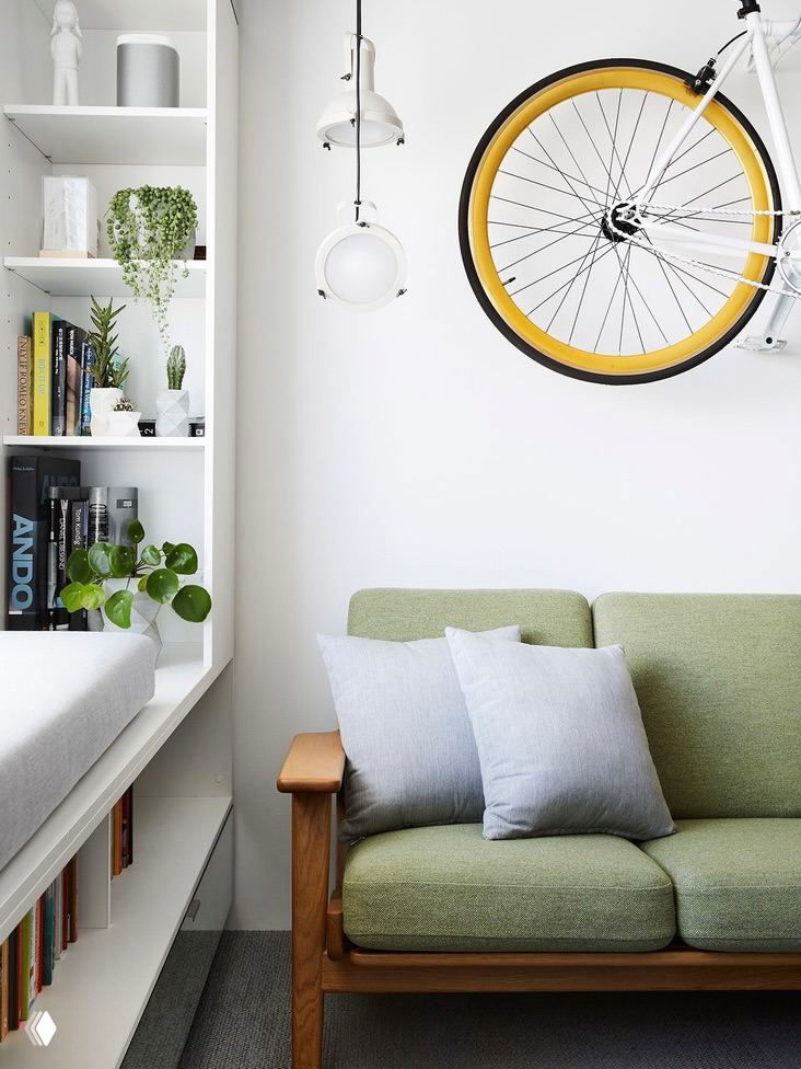 Яркий интерьер с зелёным диваном, настенными полками и подвешенным велосипедом — пример хранения спортивного инвентаря и аксессуаров на стене