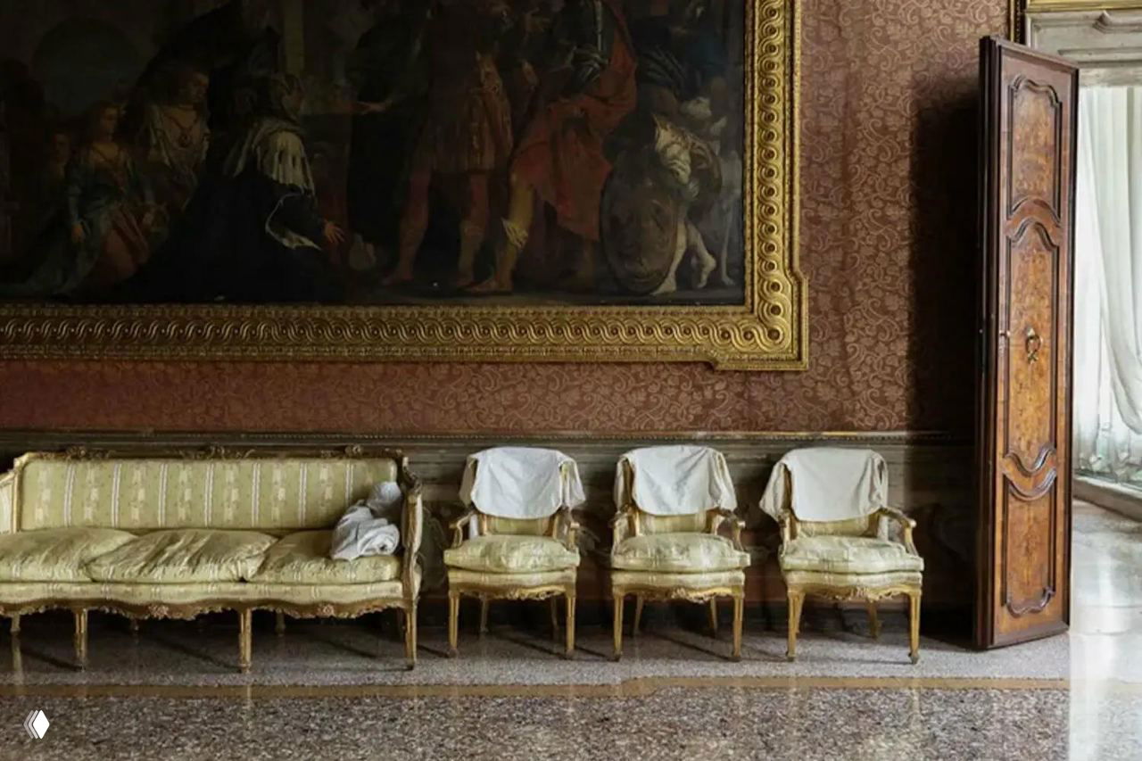 Интерьерная сцена: позолоченные диваны и стулья на фоне крупной картины в палаццо Пизани Моретта — атмосферное пространство культурного фонда.