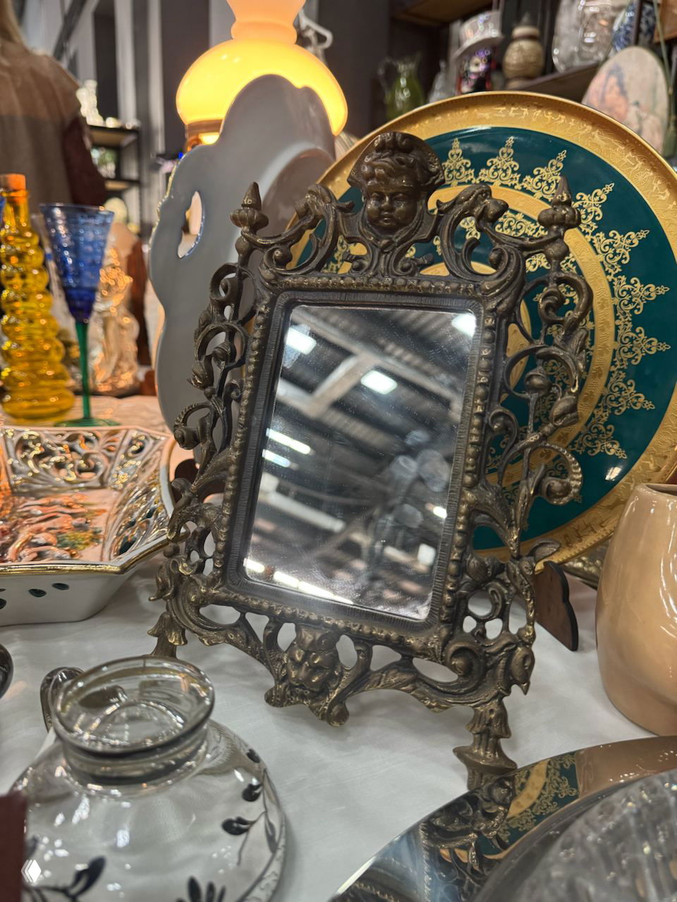 Декоративная бронзовая рамка для зеркала и коллекция различных декоративных тарелок и предметов, выставленных на маркете «Мосвинтаж».
