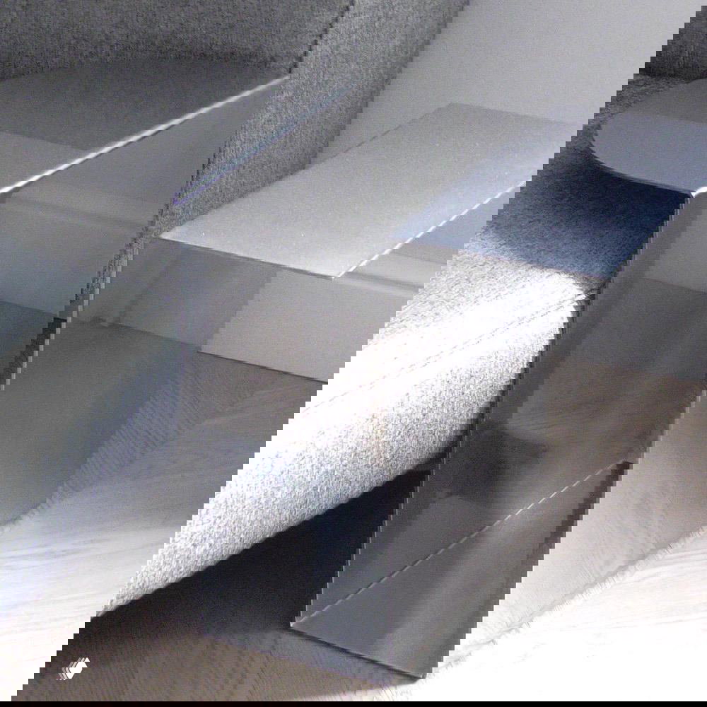 Низкий журнальный стол и подставка из нержавеющей стали с прямыми формами и зеркальной отделкой, размещённые рядом с серым диваном на паркете.