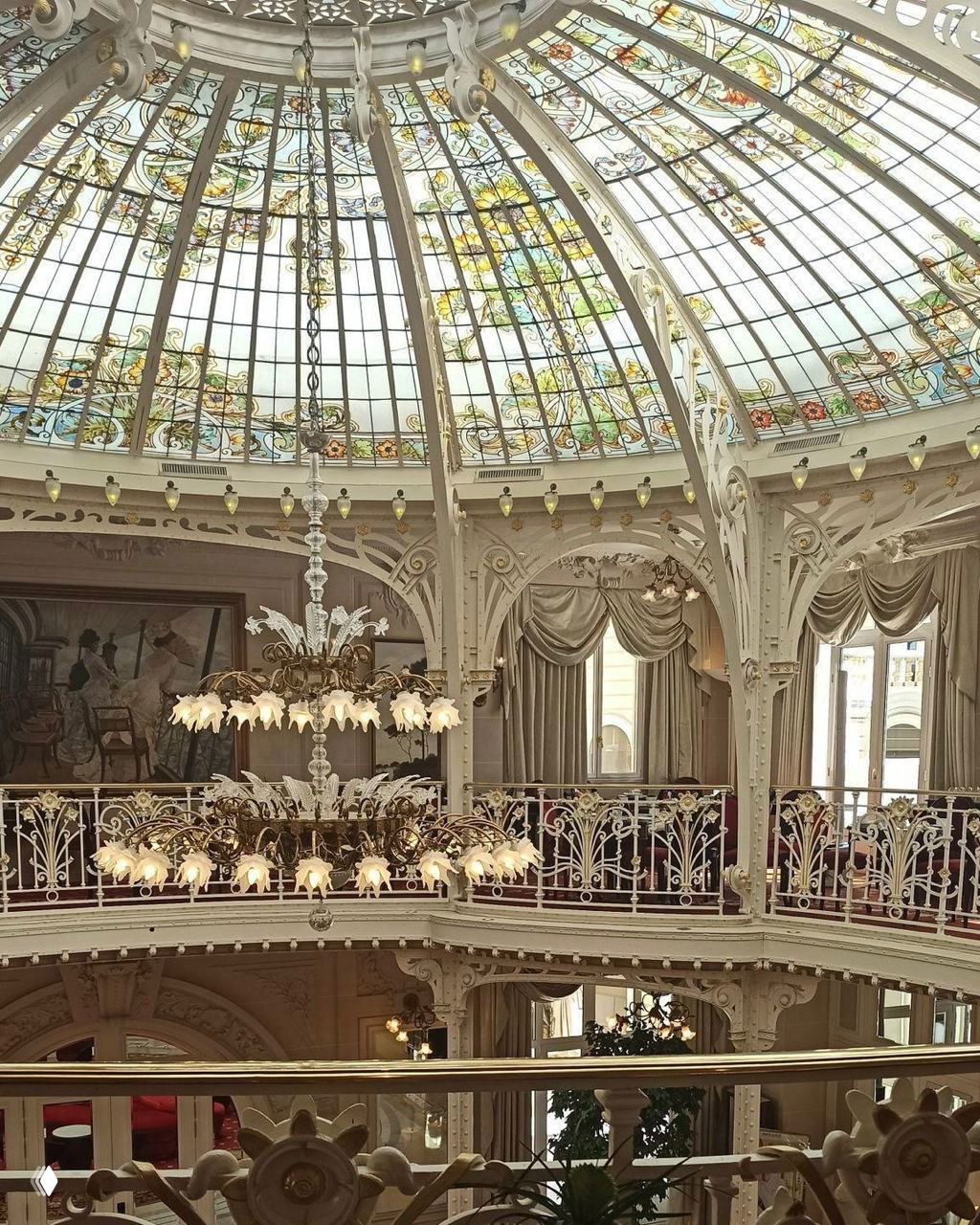 Интерьер с витражным куполом, декоративными перилами и большой люстрой в стиле модерн — богатая декоративная отделка исторического зала.