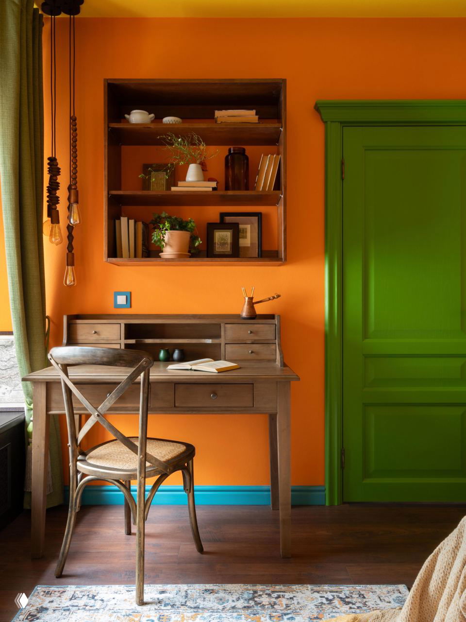 Уютный рабочий уголок с насыщенной оранжевой стеной и ярко-зелёной дверью, деревянный письменный стол, открытые полки с растениями и книгами; показан контрастный цветовой приём.