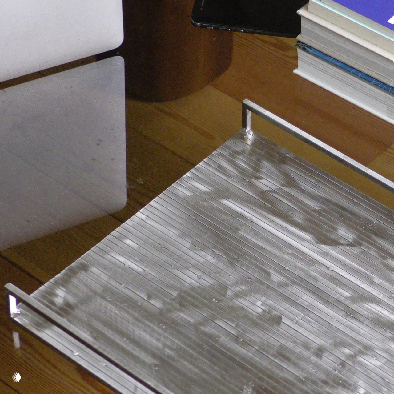 Поднос для чайных церемоний из сатинированной стали с рифлёной фактурой, стоящий на столе рядом с книгами и аксессуарами.