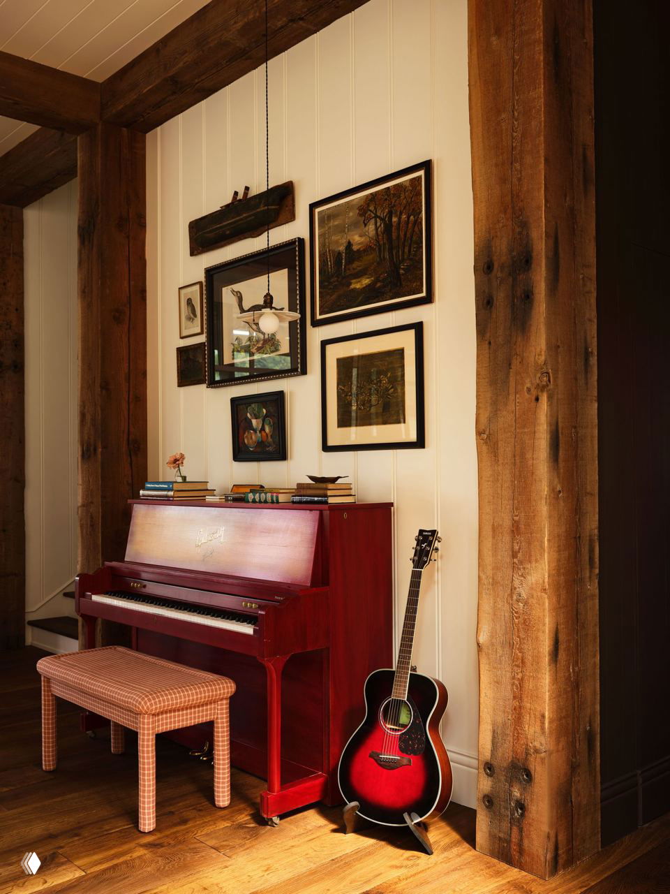 Угол с роялем и гитарой, оформленный деревянными балками и галереей картин на стене; винтажные предметы как элемент интерьерной композиции.