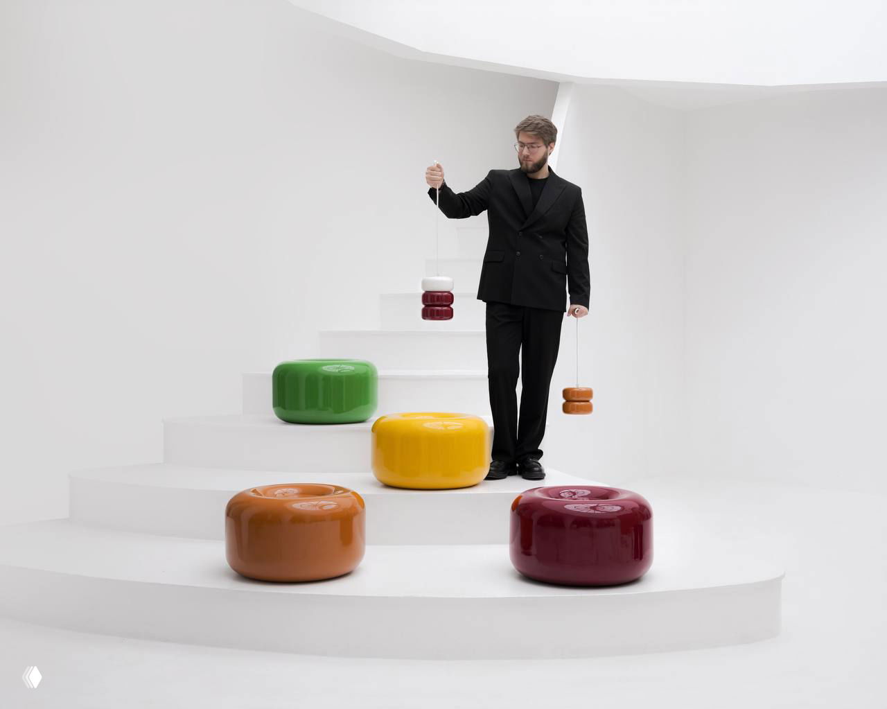 Дизайнер держит в руках подвесной модуль коллекции Caramel, на ступенях расположены крупные керамические пуфы-столики разных цветов на нейтральном фоне.