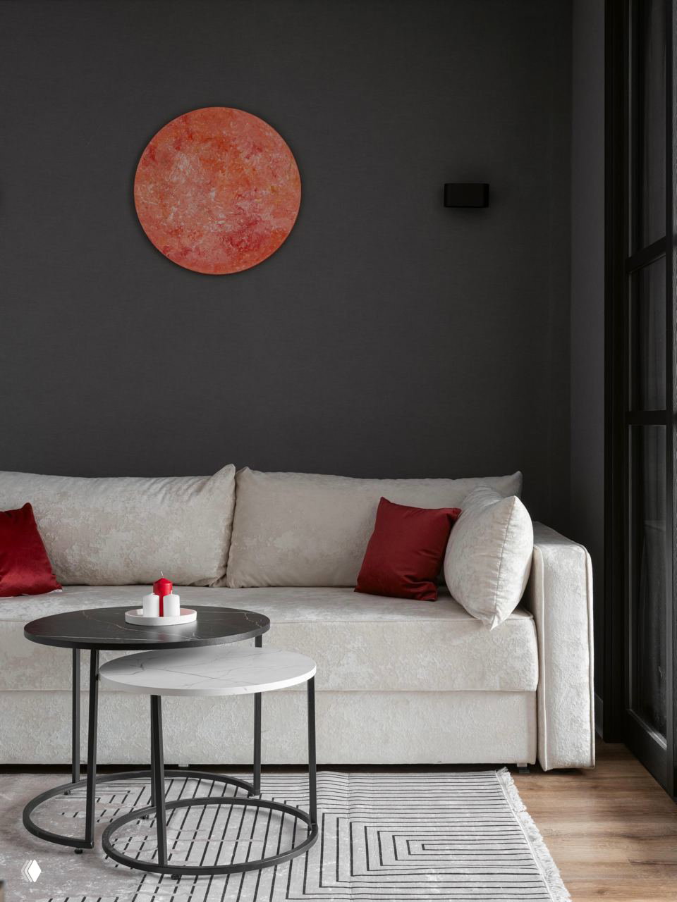 Крупный план светлого дивана с бордовыми декоративными подушками на фоне тёмной стены и круглой абстрактной картины, уютный ковер на полу.