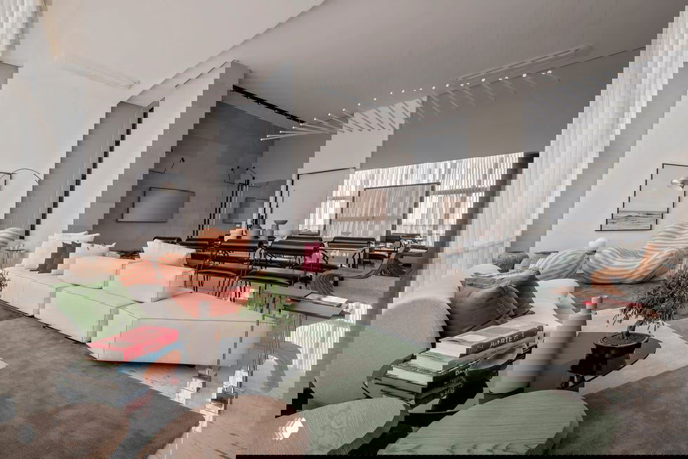 Большая открытая гостиная-студия с модульным белым диваном, зелёным ковром, декоративными креслами и отражающим мраморным покрытием пола.