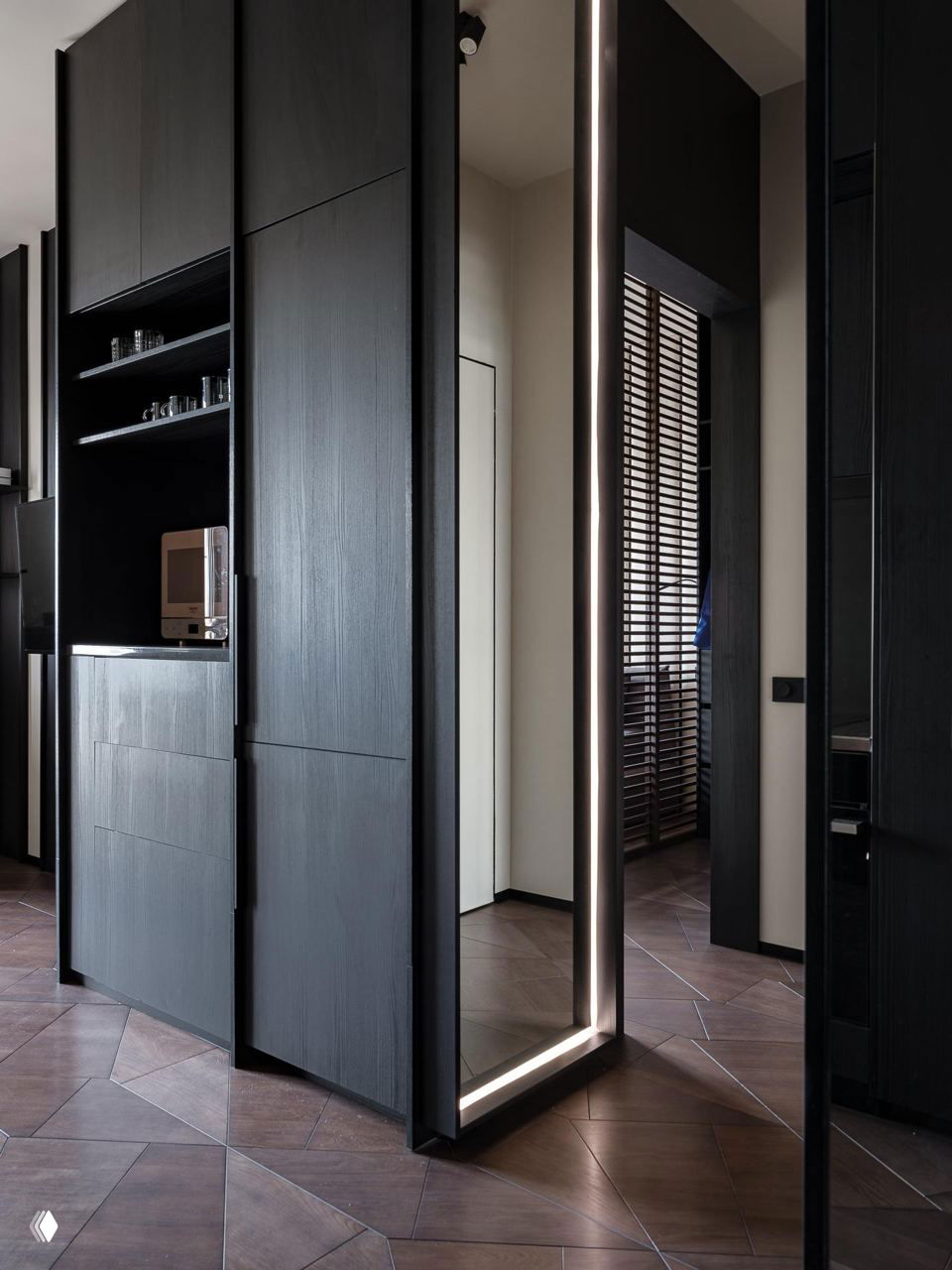 Высокие тёмные встроенные шкафы и большое зеркало с подсветкой: переходы от хранения к открытому пространству в компактной планировке.