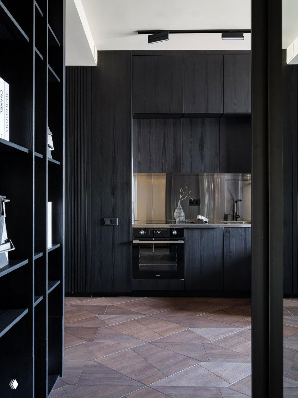 Чёрная кухонная мебель и встроенная техника на фоне геометрического паркета: строгие фасады и металлический фартук создают брутальный акцент.