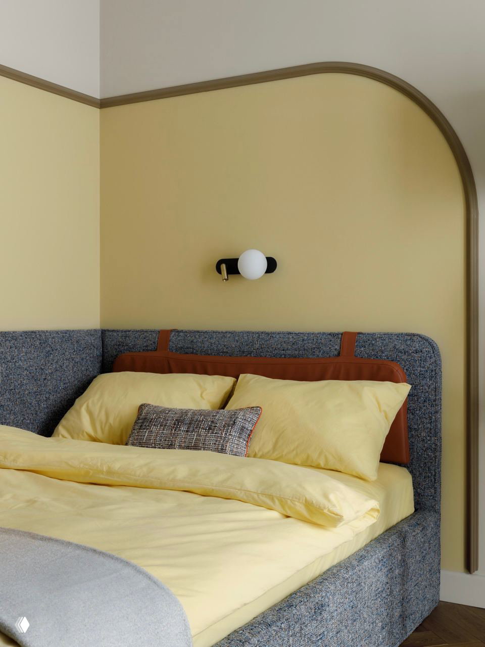 Нейтральная гостевая спальня с мягким серым изголовьем, жёлтыми стенами и арочным молдингом, аккуратное настенное бра создаёт мягкий приглушённый свет.