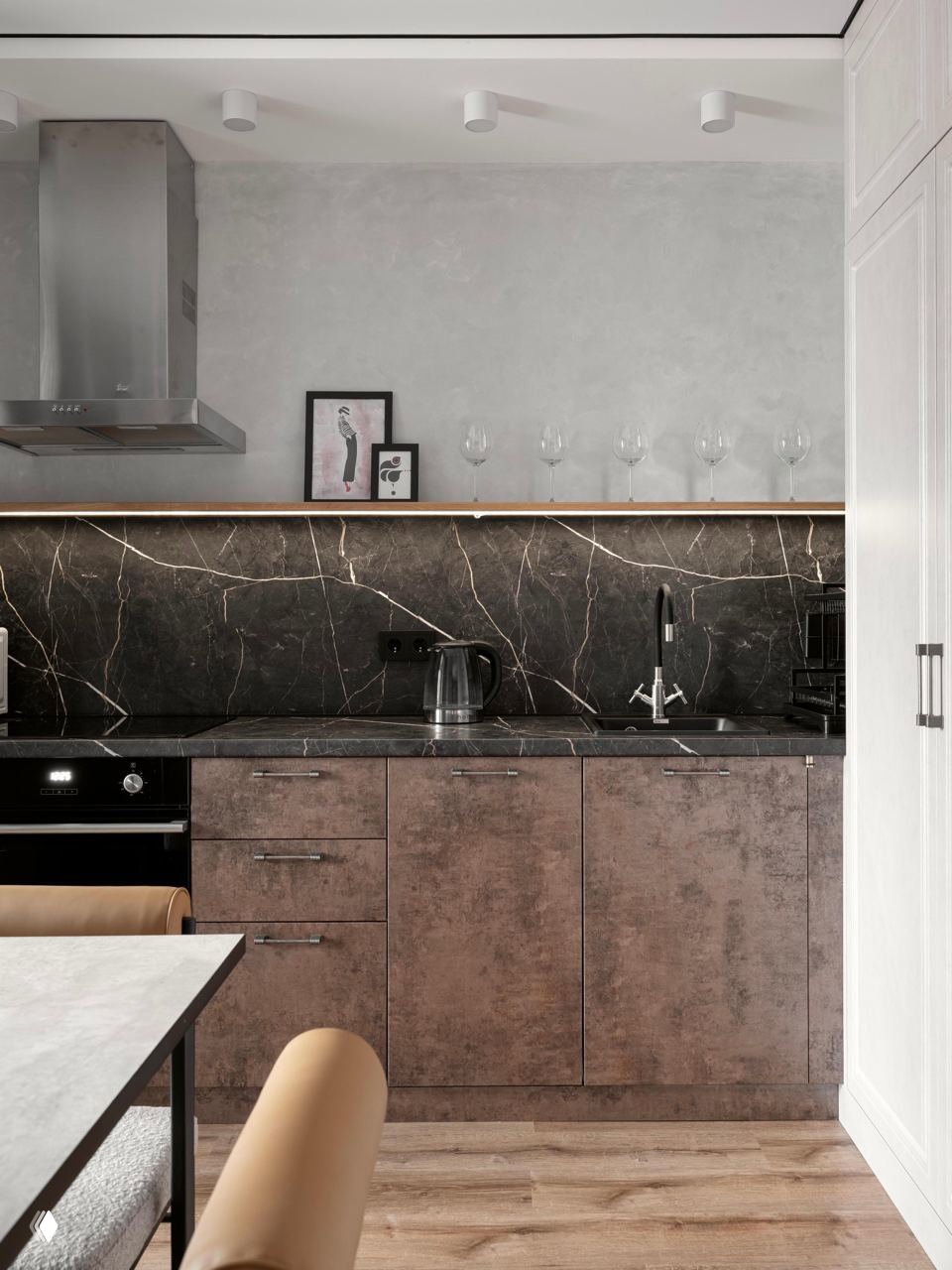 Кухонный гарнитур с тёмной мраморной столешницей и фартуком, верхняя полка со стеклянными бокалами и встроенная вытяжка над рабочей зоной.