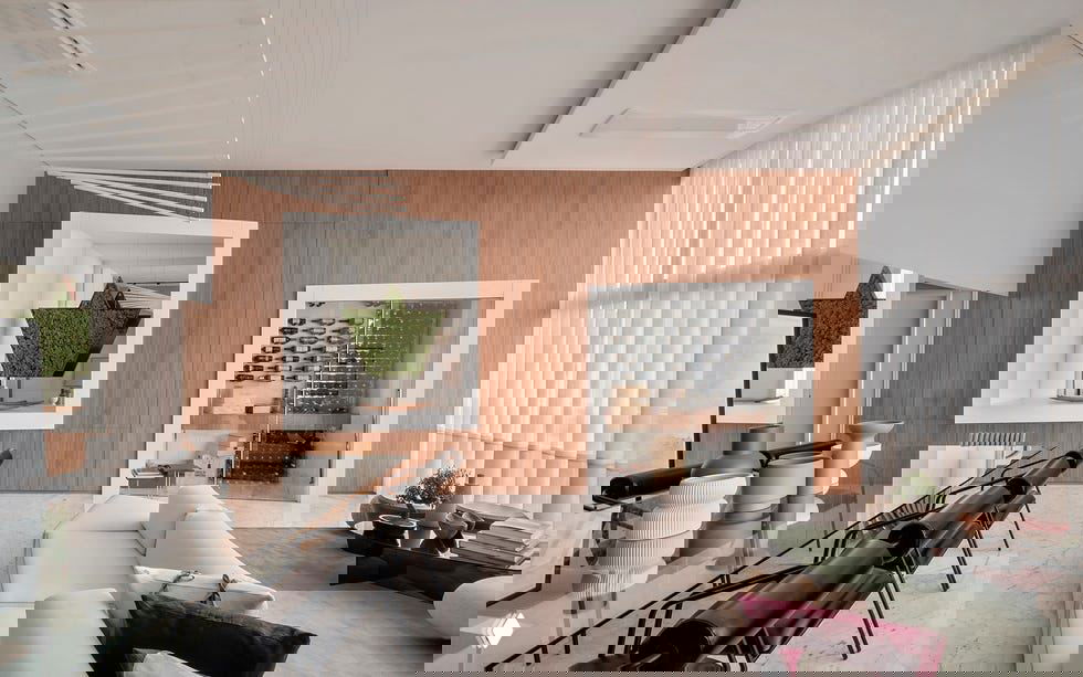 Столовая зона с длинным стеклянным столом, чёрными стульями, деревянной стеной и встроенной винной витриной на фоне светлого мраморного пола.