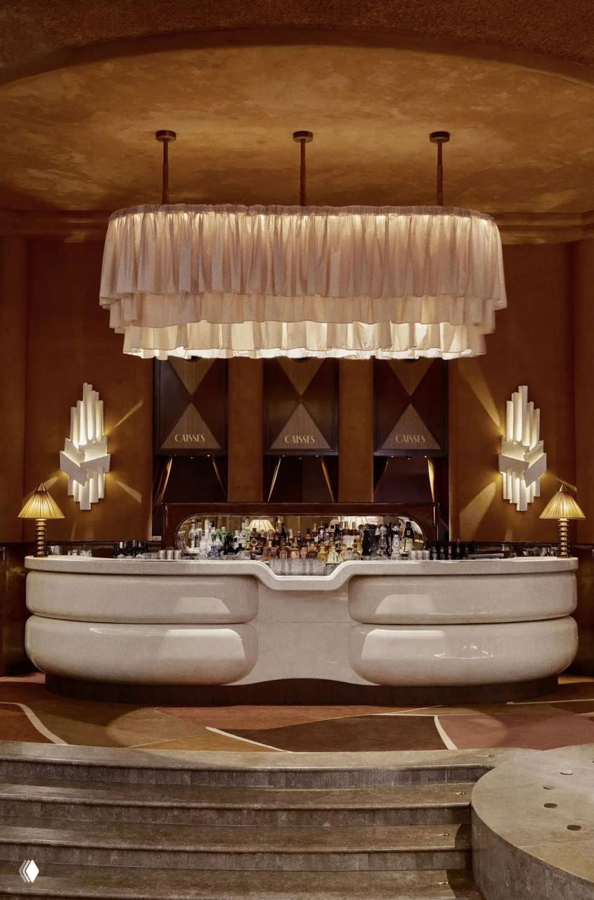 Барная зона с крупной многослойной люстрой и плавными меблированными формами — сочетание ретро-эстетики 1920–1950-х годов.