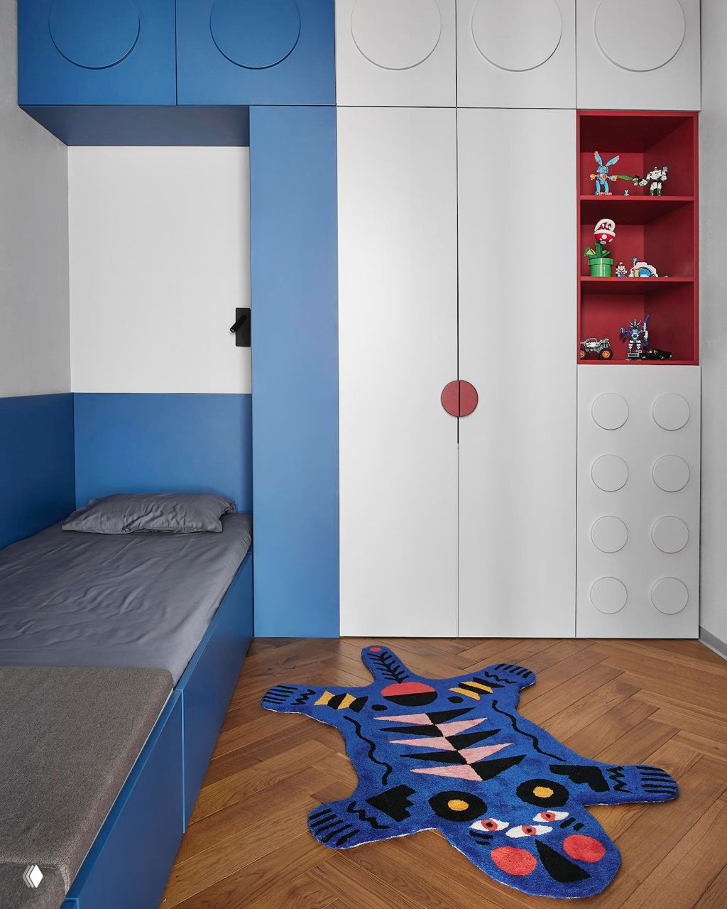 Фрагмент детской в синих и белых тонах: встроенные шкафы, игровый коврик в форме животного и минималистичное спальное место у стены.