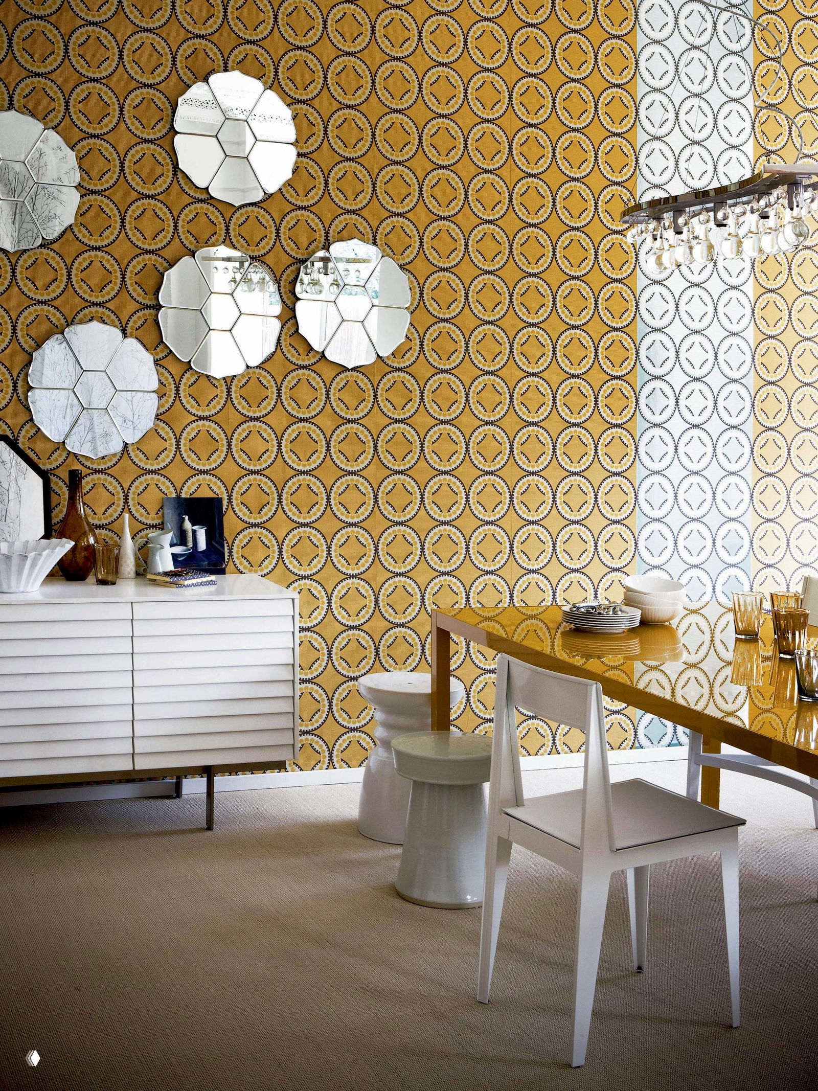 Современная столовая зона с узорными обоями жёлтого тона и зеркальными декоративными элементами на стене, стеклянный стол и светлая мебель.
