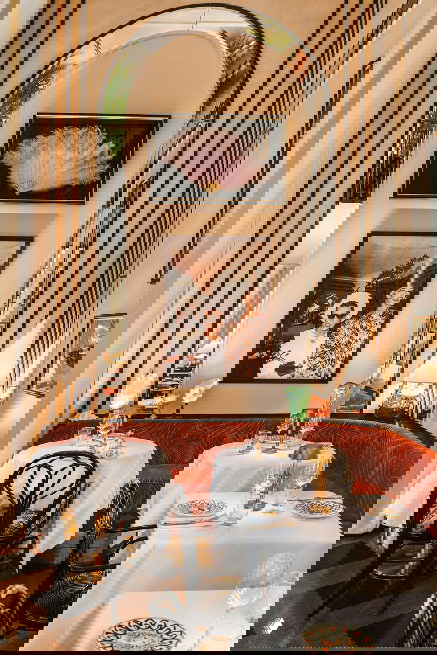 Уютный столик у арки: арочная ниша с произведениями искусства, столы со скатертями и высокая вертикальная композиция в интерьере Gloria Osteria.