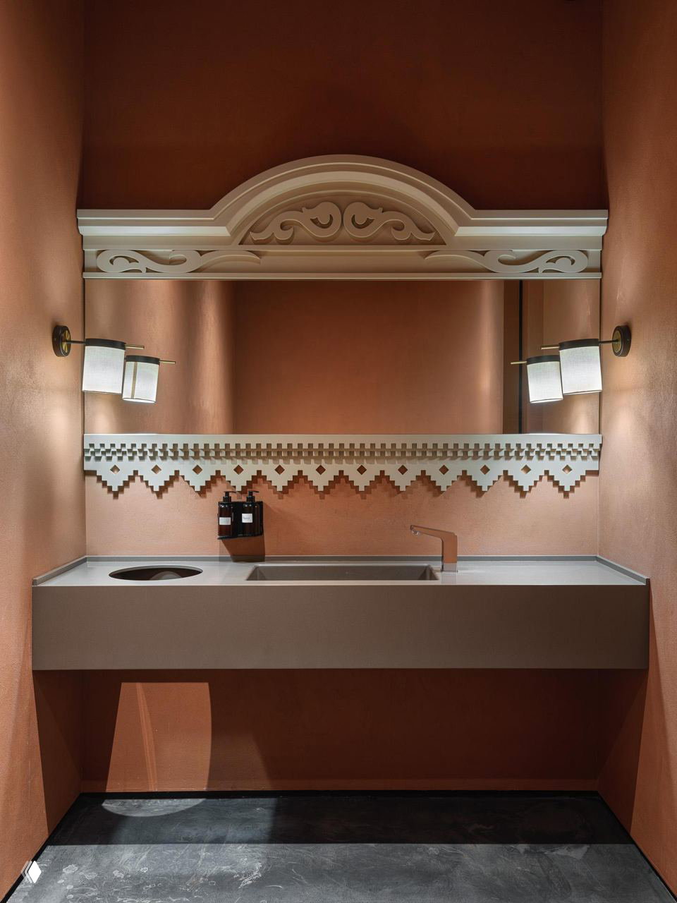 Санузел или зона с раковиной в тёплой терракотовой гамме, зеркало с резной верхней накладкой и декоративным пиксельным бордюром из плитки.