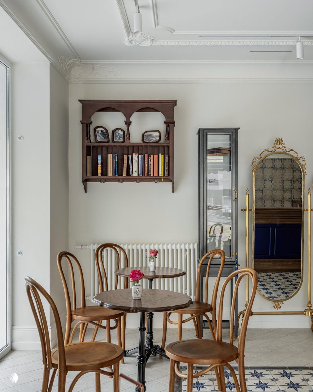 Уютный уголок с круглыми столиками и венскими стульями, настенная полка с книгами, старинное зеркало и лепнина на стене.