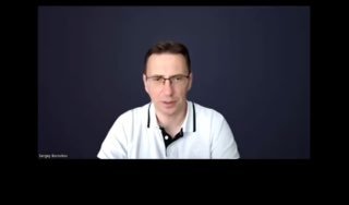 Скриншот видеозаписи вебинара: мужчина в белой рубашке на тёмном фоне объясняет условия программы, крупный план лица и плеч.
