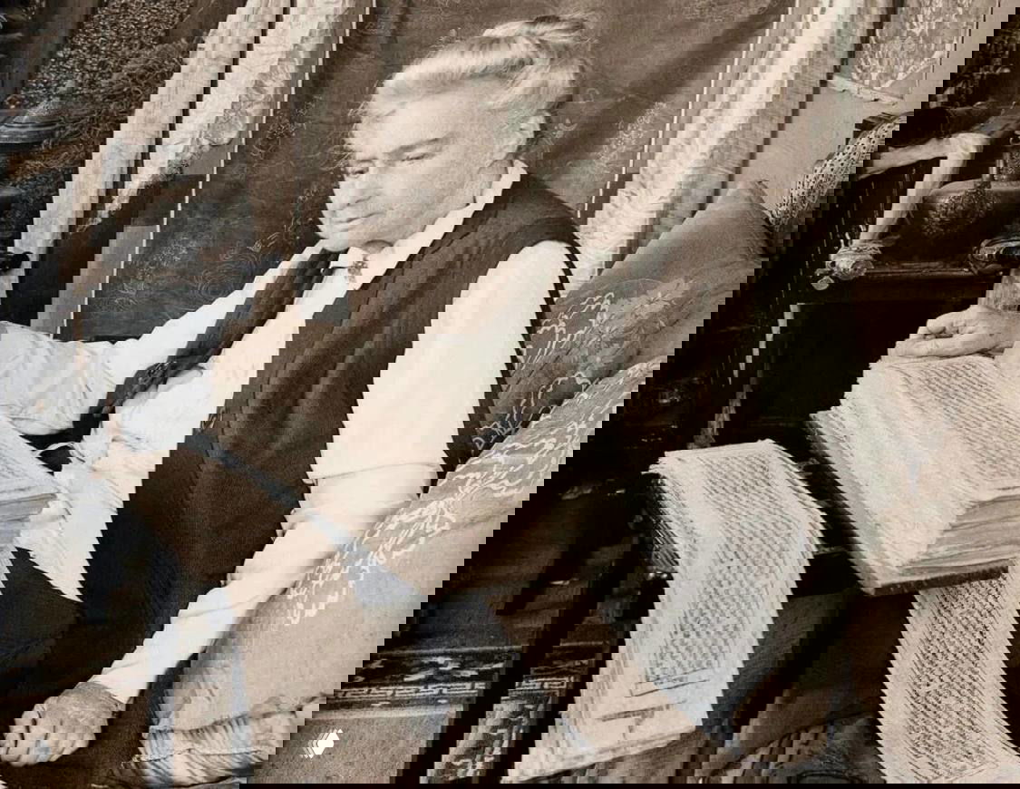 Александра Давид-Неель в зрелом возрасте за изучением тибетских манускриптов и свитков в интерьере — историческое фото, демонстрирующее её научные интересы.