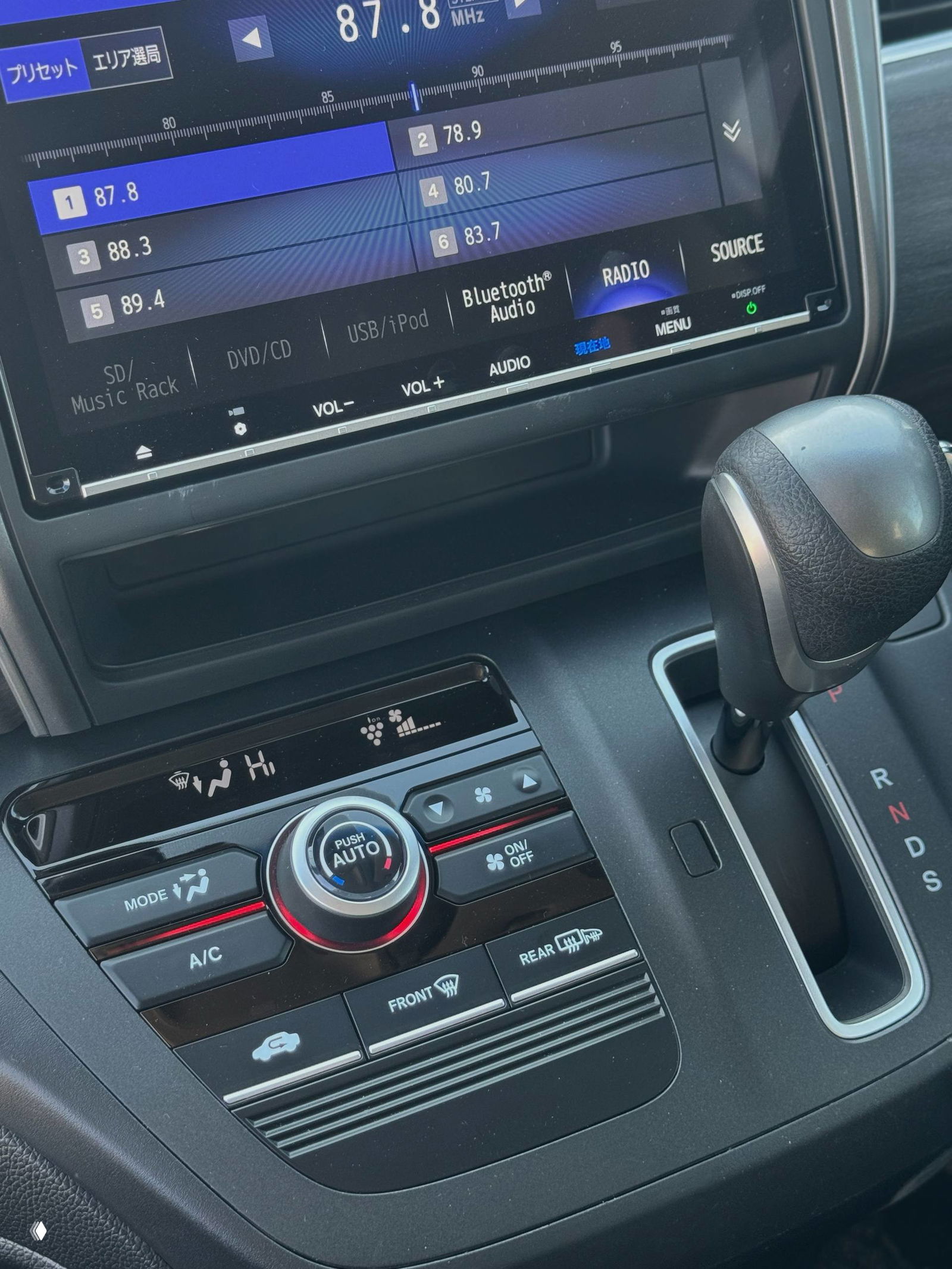 Крупный план центральной консоли Honda Freed: мультимедийный дисплей, радиочастоты, элементы управления климатом и рычаг вариатора, чистый салон.