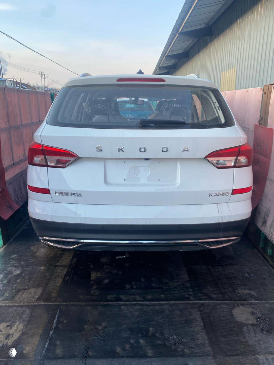 Задняя часть белой Skoda Kamiq на платформе: видно багажник и шильдики модели, машина готовится к отправке в Россию.