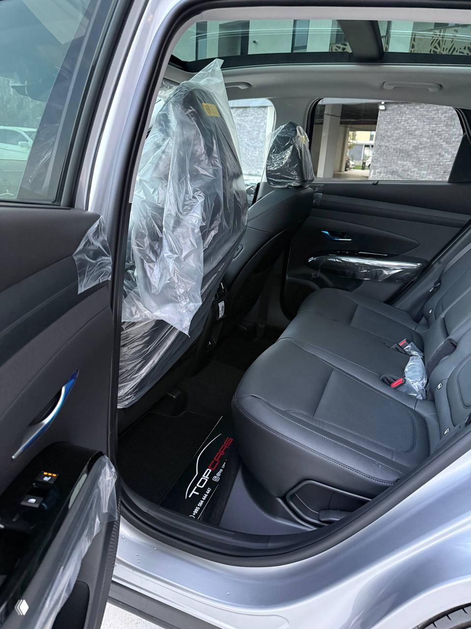 Интерьер Hyundai Tucson: задние кожаные чёрные сиденья с защитной плёнкой на подголовниках и вид на панорамную крышу из салона.