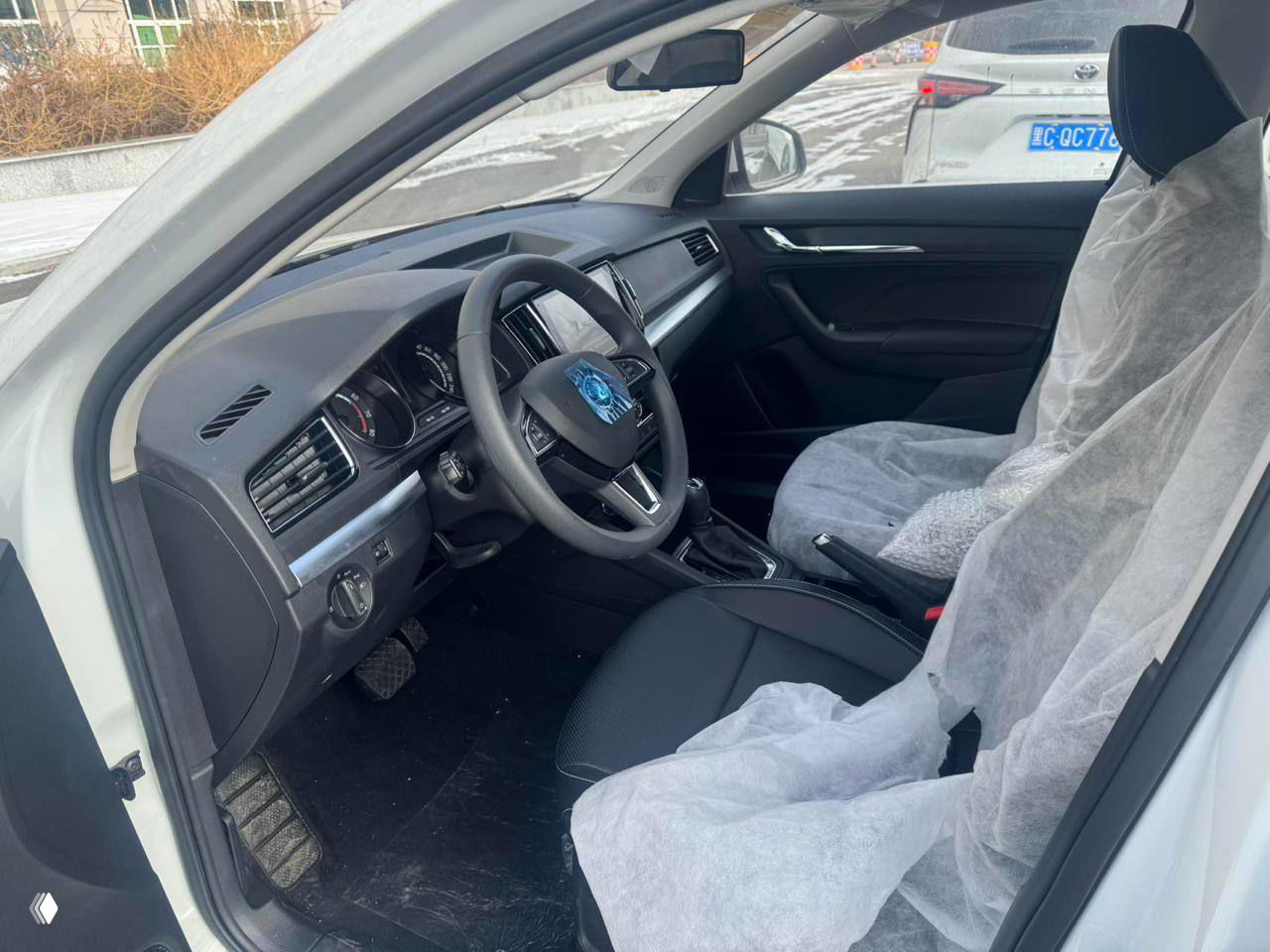 Салон Skoda Kamiq: переднее пассажирское место и панель приборов, сиденья закрыты защитными чехлами, состояние нового автомобиля.