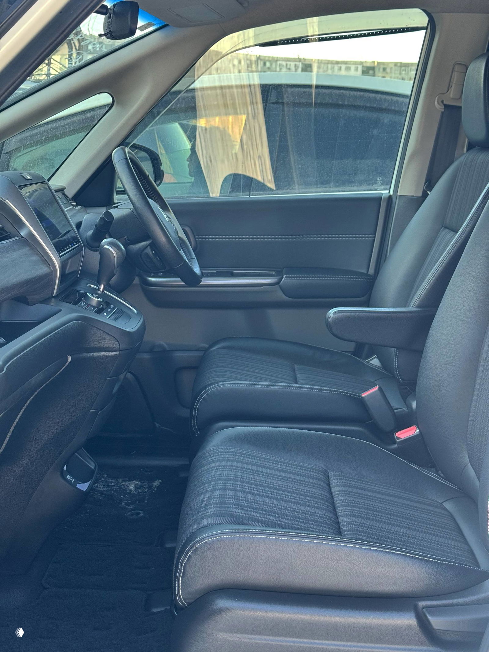 Передние сиденья и водительская зона Honda Freed: чёрная обивка с контрастной прострочкой, подлокотник, руль и дверная панель, аккуратный салон без видимых повреждений.