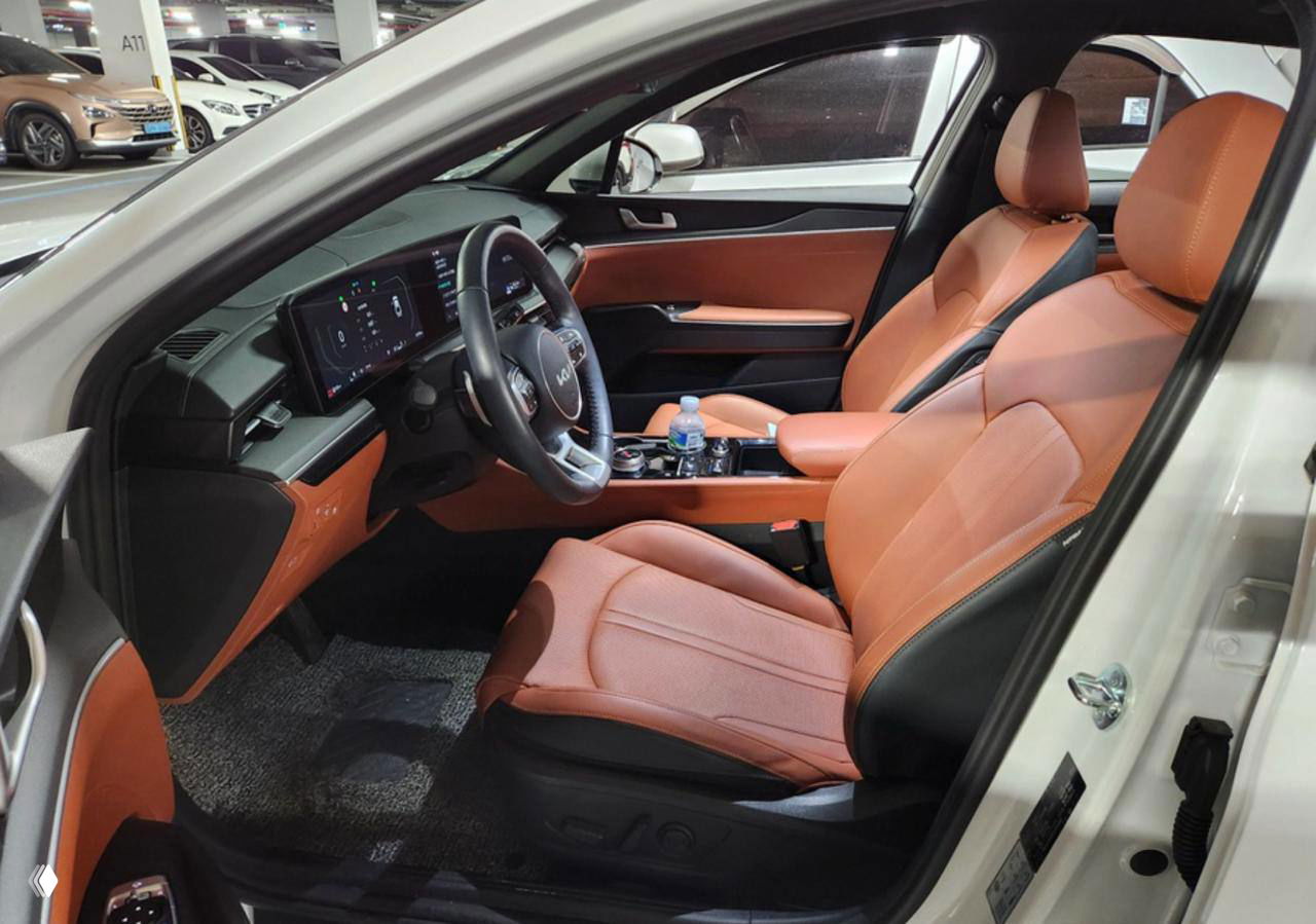 Фото передних сидений KIA K5 с оранжевой кожаной отделкой; демонстрация состояния обивки, подлокотников и посадочного места для отчёта.