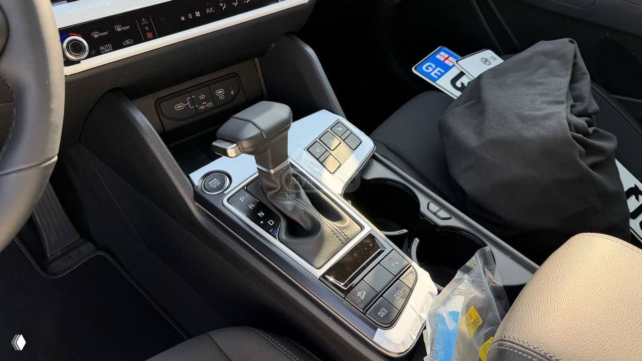 Крупный план центральной консоли KIA Sportage 2025: селектор АКПП, элементы управления и подстаканники, защитная плёнка на элементах.