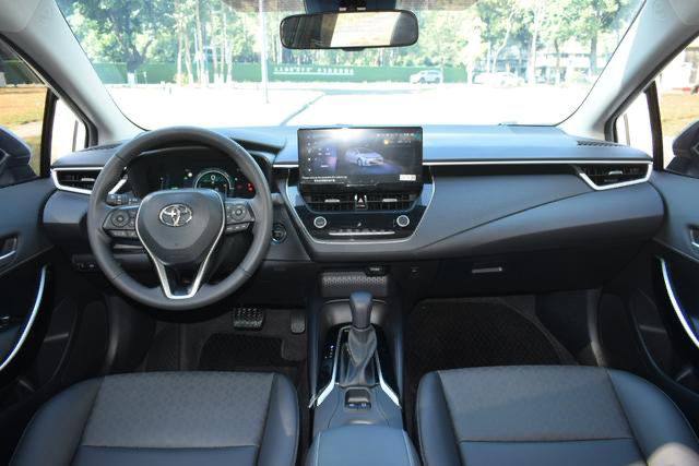 Салон Toyota Corolla Hybrid 2025: передняя панель с трехспицевым рулем, мультимедийный экран и приборная панель в дневном свете.
