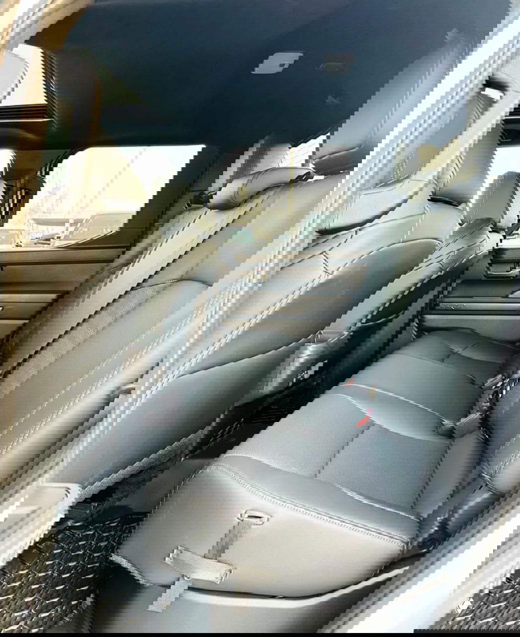 Интерьер Toyota Tacoma: задний ряд сидений с кожаной обивкой, ремнями безопасности и панорамной крышей, чистый салон и вид через окна на парковку.