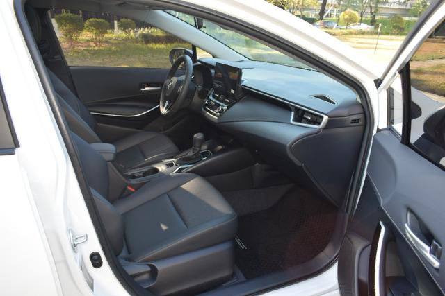 Вид на передний пассажирский отсек Toyota Corolla Hybrid: сиденье, открытая дверь и торпедо — салон в ухоженном состоянии.