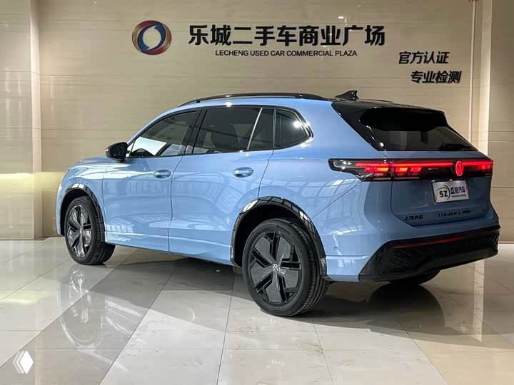 Голубой Volkswagen Tiguan L Pro — вид сзади‑слева в шоуруме, заметна современная светотехника и багажник автомобиля.