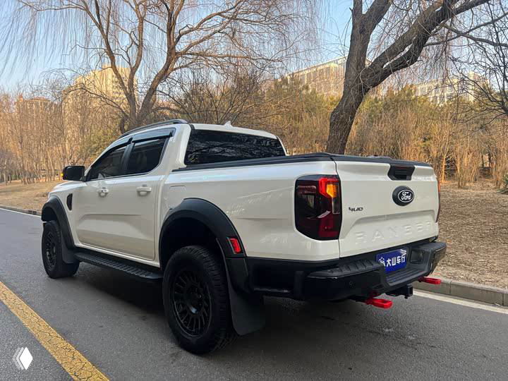 Пикап Ford Ranger, вид сзади-угла; открытая платформа кузова, задние фонари и буксировочные крюки, автомобиль на асфальтовой дороге у парковой зоны.