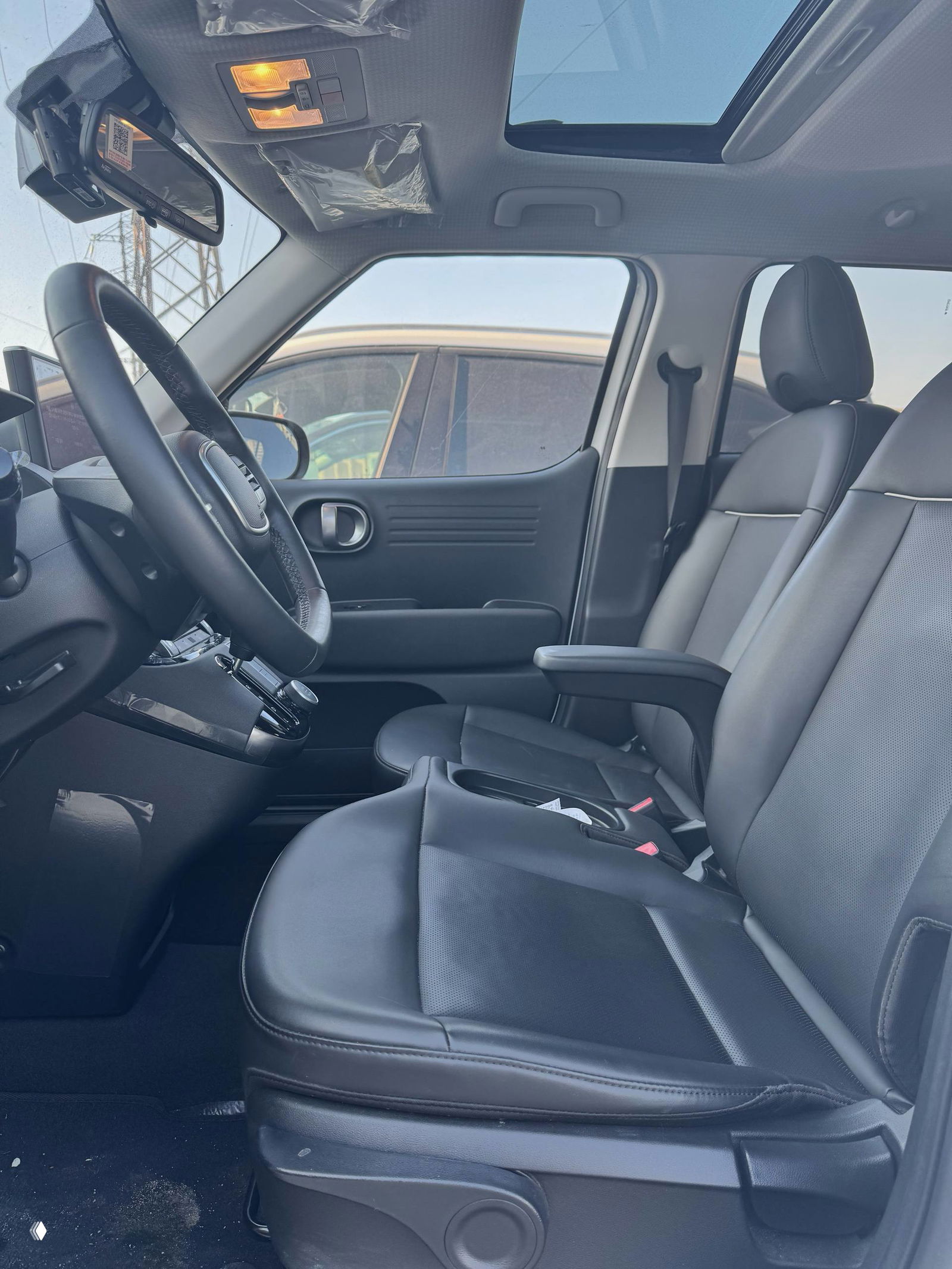 Передние сиденья Hyundai Casper в кожаной обивке, вид сбоку через водительскую дверь: подлокотник, панорамный люк над сиденьями и чистый салон без повреждений.