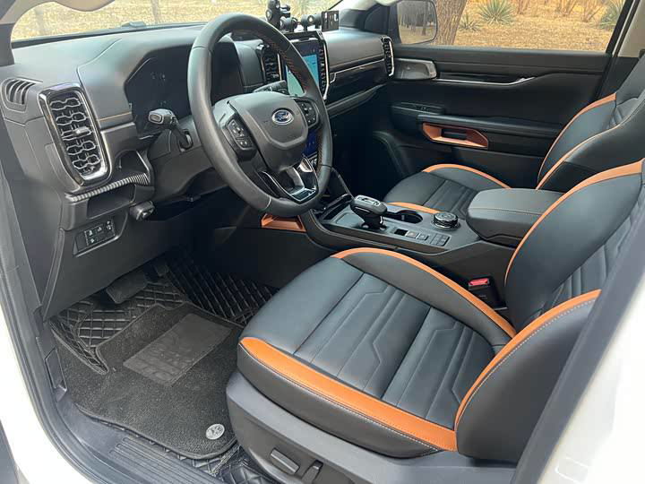 Передние сиденья пикапа Ford Ranger с контрастной оранжевой прострочкой, кожаная обивка и удобные подлокотники, вид со стороны пассажирской двери.