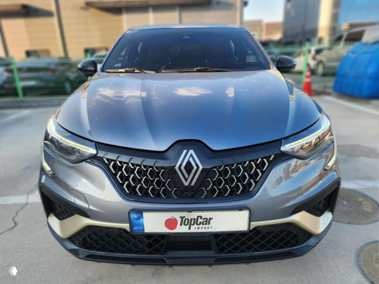 Серебристый Renault Arkana E‑Tech крупным планом: фасадная решётка, эмблема Renault и номерная пластина с логотипом TopCar на парковке.