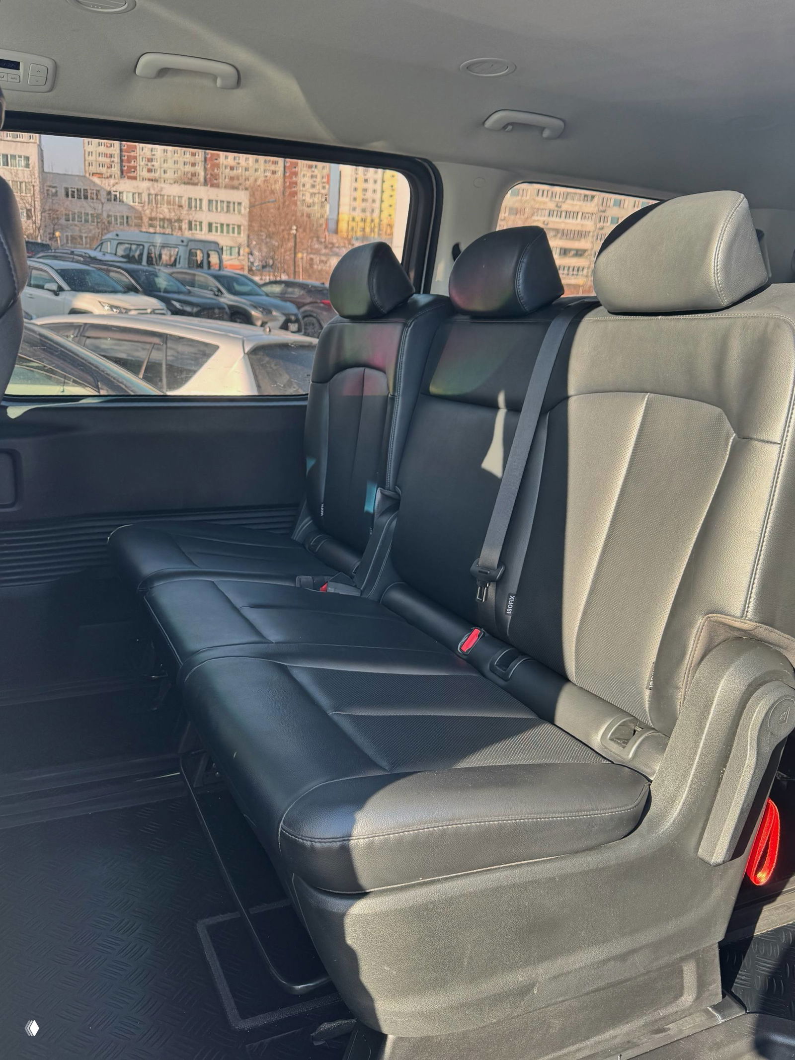 Задний трёхместный ряд сидений Hyundai Staria — кожаная скамья, ремни безопасности и окно с видом на парковку, простор для пассажиров.