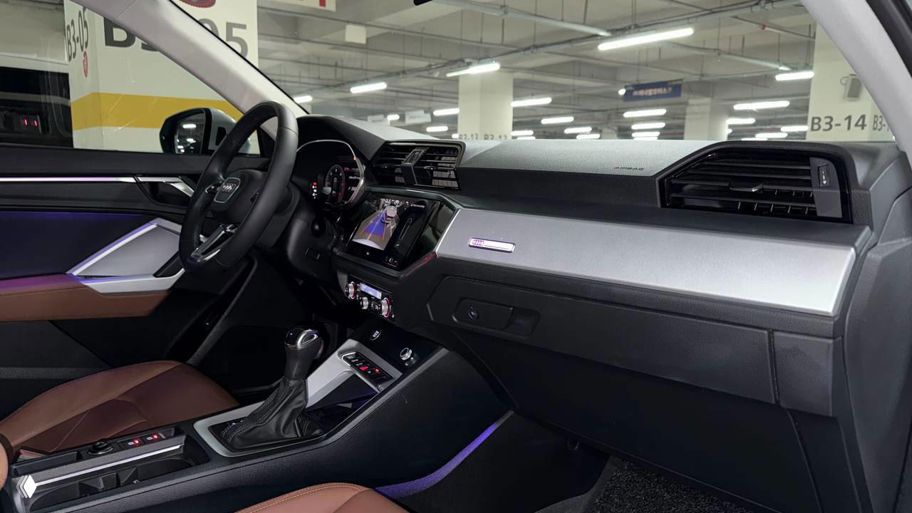 Интерьер Audi Q3 или аналогичного кроссовера: торпедо, мультифункциональное рулевое колесо и информационный экран, фото в крытой парковке.