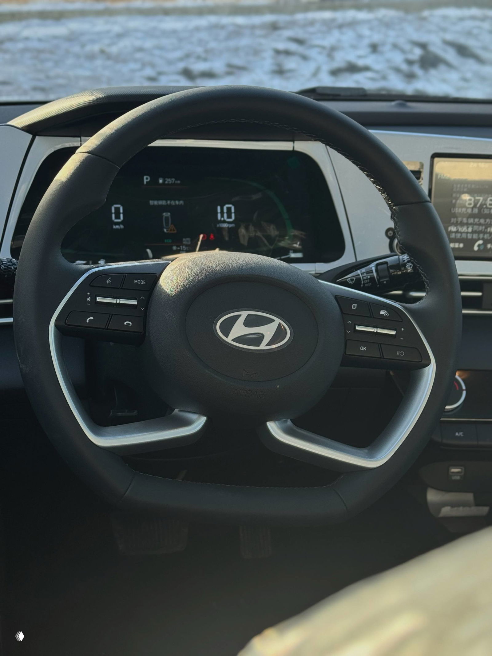 Крупный план рулевого колеса Hyundai с эмблемой, видно цифровую приборную панель и элементы управления — интерьер нового автомобиля.