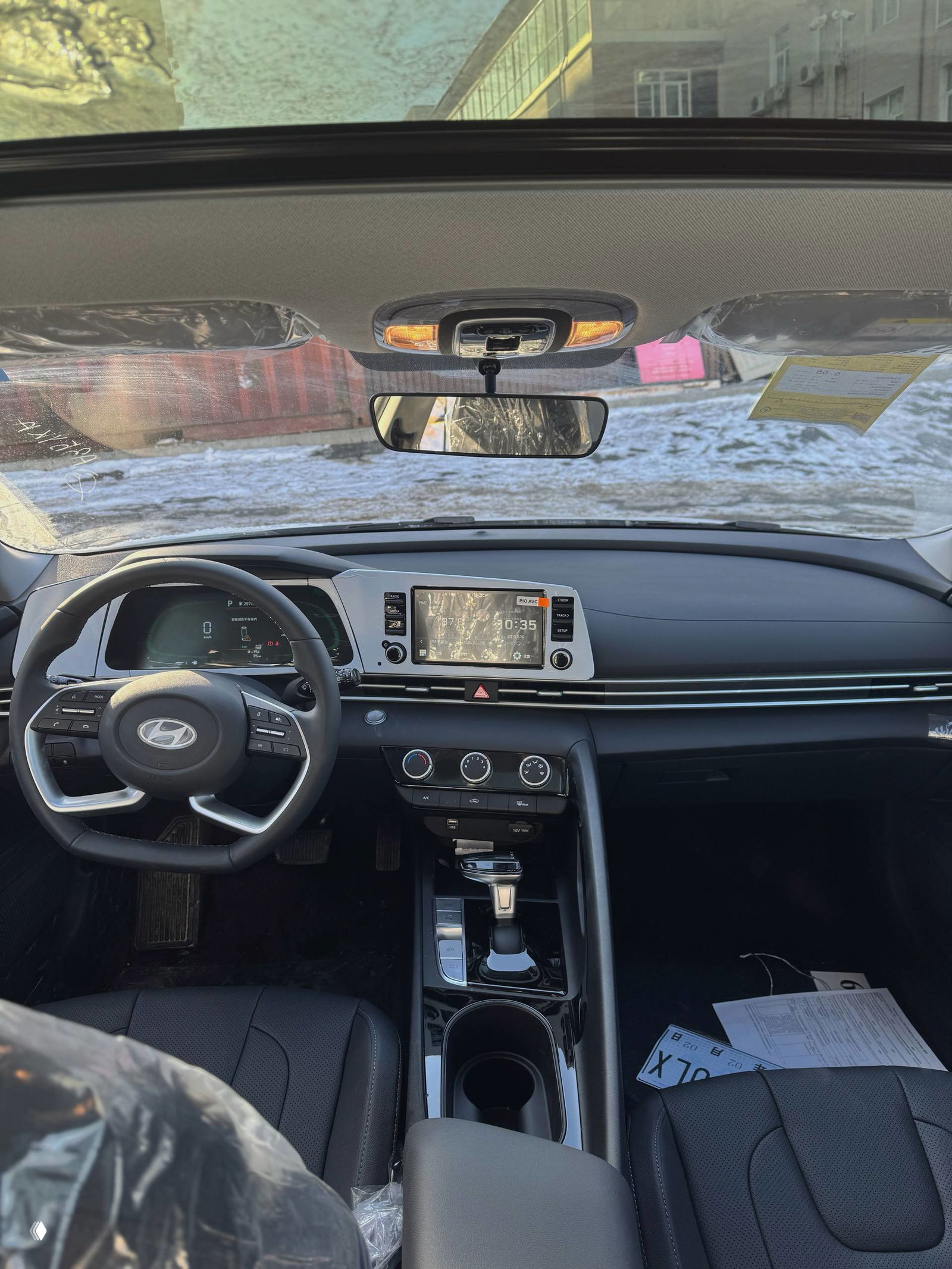 Широкий вид на переднюю часть салона Hyundai Elantra: руль, центральная консоль, селектор передач и обзор лобового стекла снаружи.