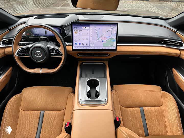 Интерьер Mazda EZ-6: панорамный вид на руль, центральный дисплей и передние сиденья в коричнево-замшевой отделке, просторный салон.