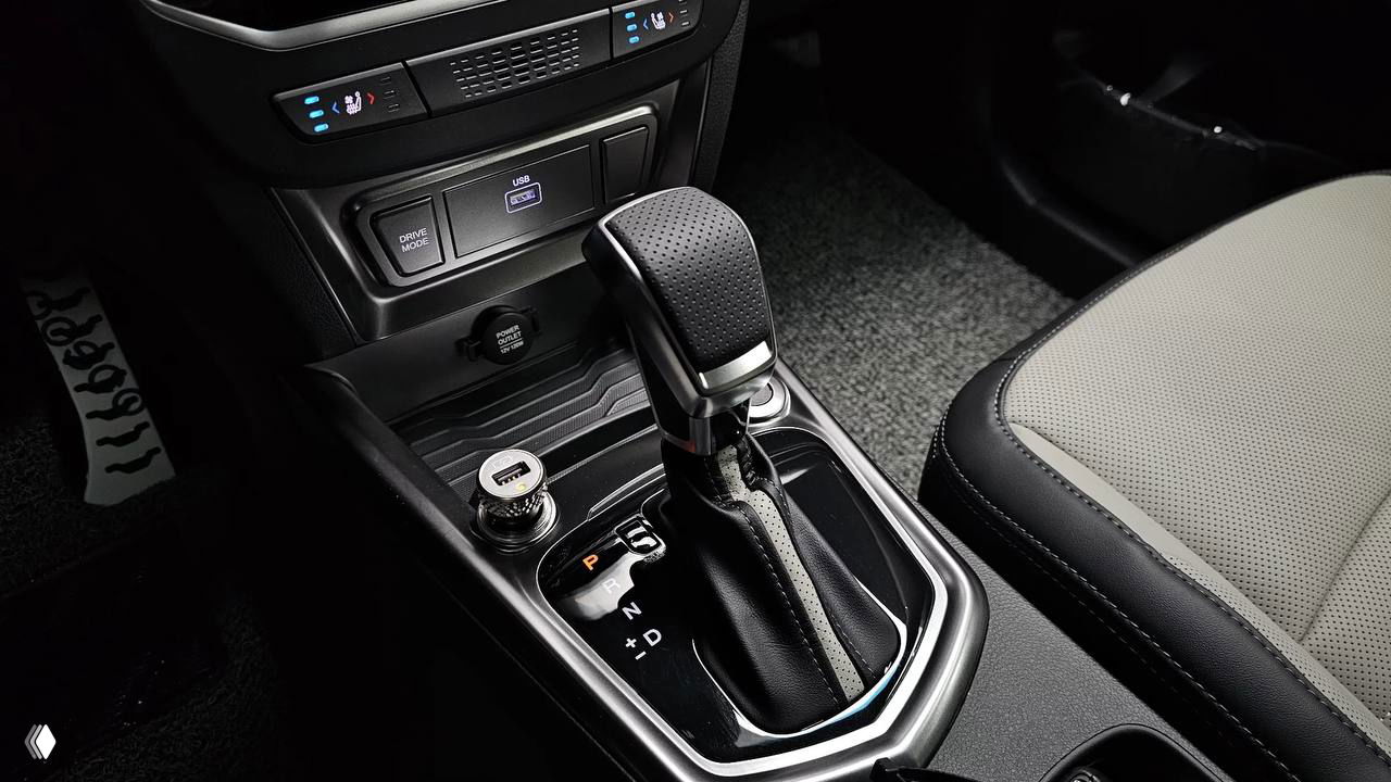 Крупный план селектора автоматической коробки передач и зоны центрального тоннеля в SsangYong Tivoli 2026, видны подстаканники и розетка USB.