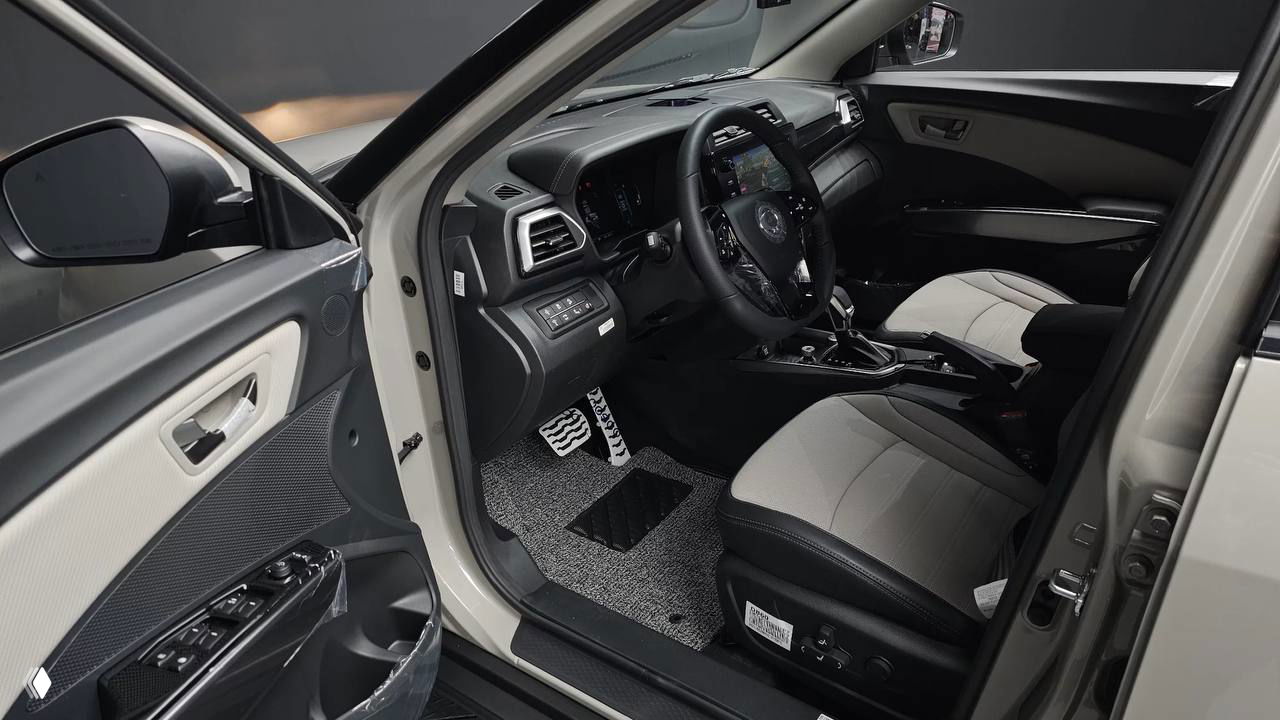 Вид водительской двери и переднего посадочного места SsangYong Tivoli 2026 с открытой дверью, видно панель управления стеклоподъёмниками и обшивку салона.