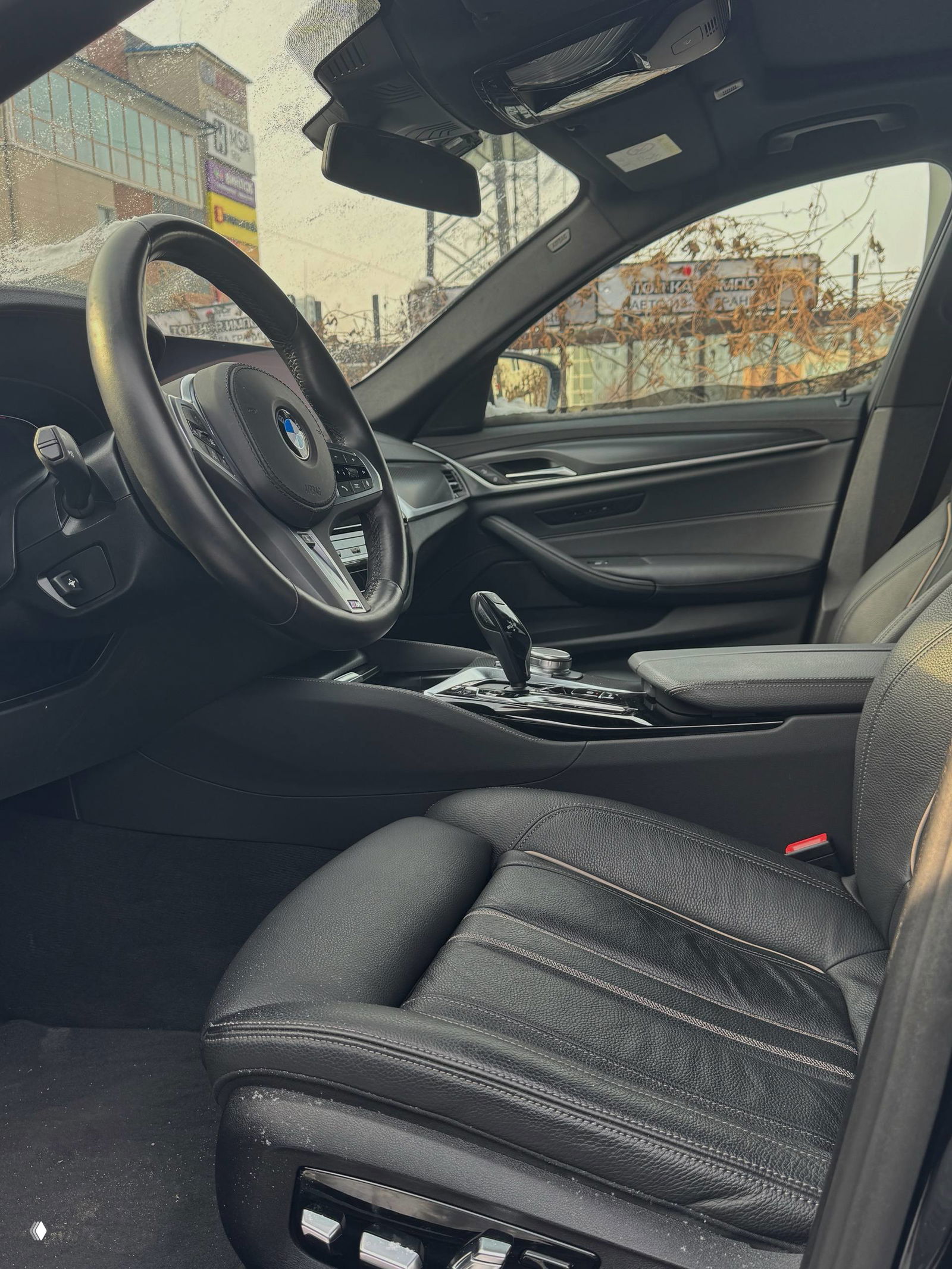 Водительское кресло BMW 520i: кожаная отделка сиденья, регулировки на боковой панели и общий вид передней посадочной зоны в зимних условиях.